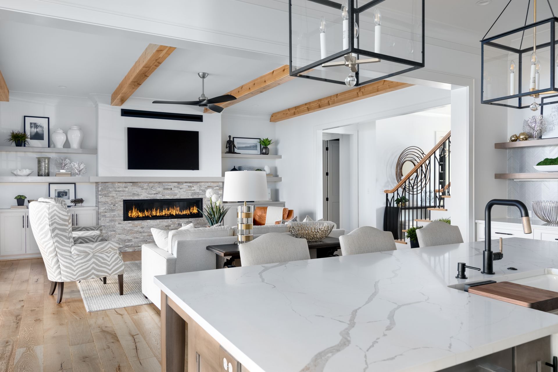 Bright modern living room and kitchen with white decor, fireplace, island, and black-framed pendant lights