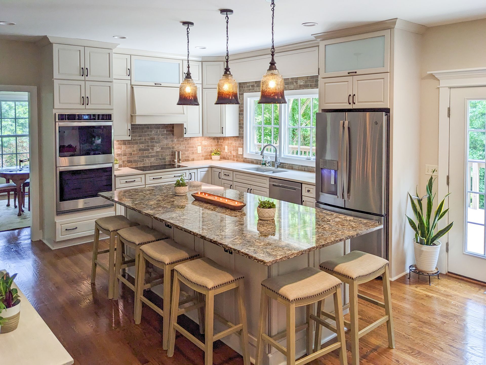 Modern kitchen with granite island, pendant lights, wooden stools, and stainless steel appliances