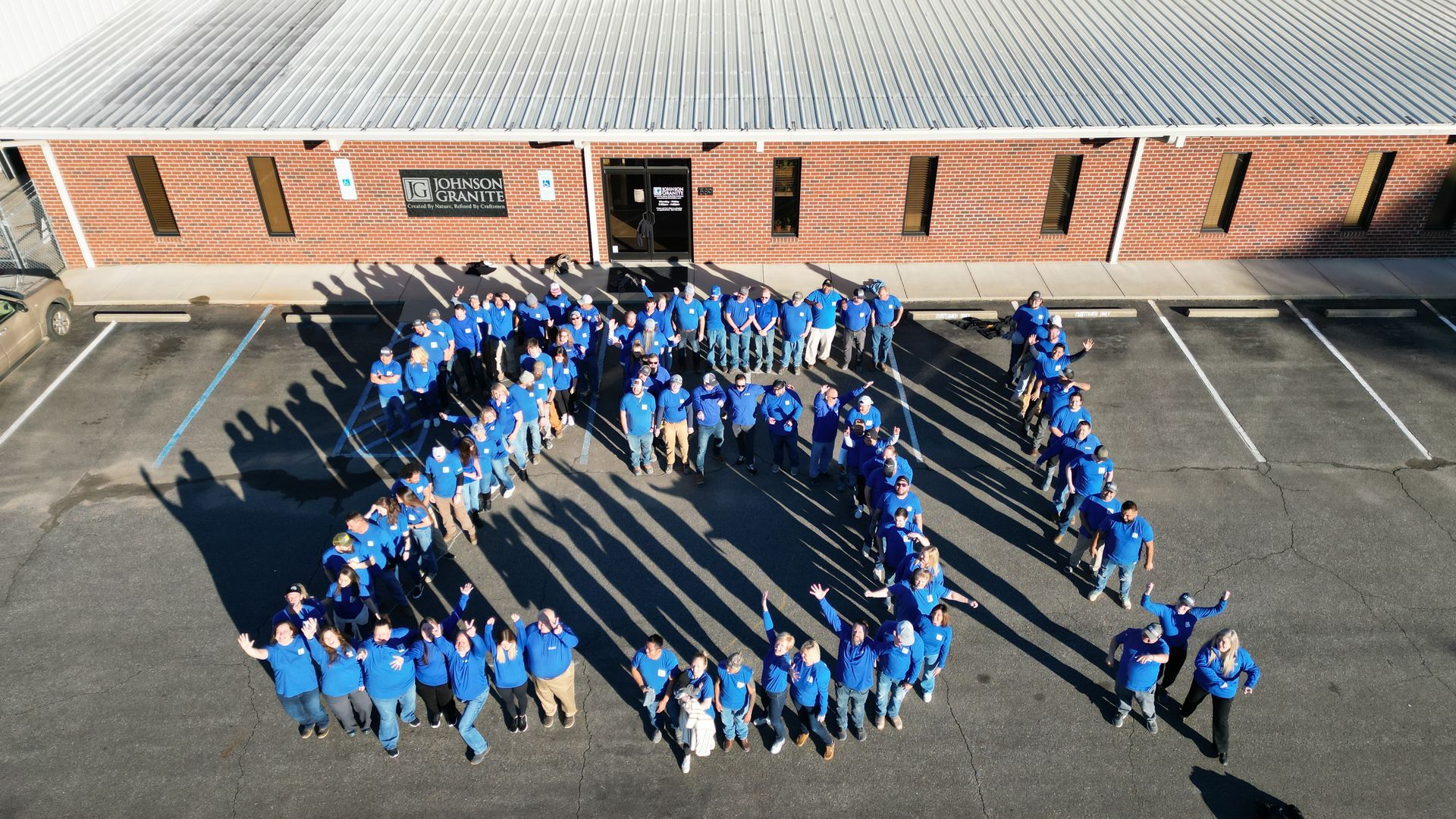 People in blue shirts form a large ring outside a brick building, seen from above.