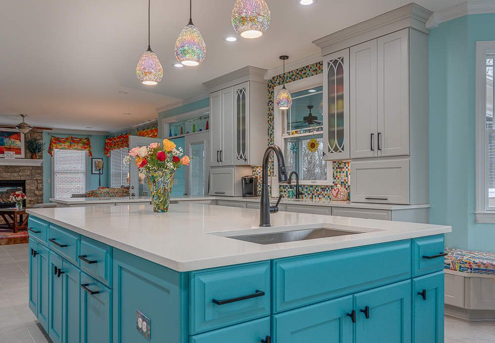Bright modern kitchen with turquoise island, white countertops, pendant lights, and a vase of flowers.