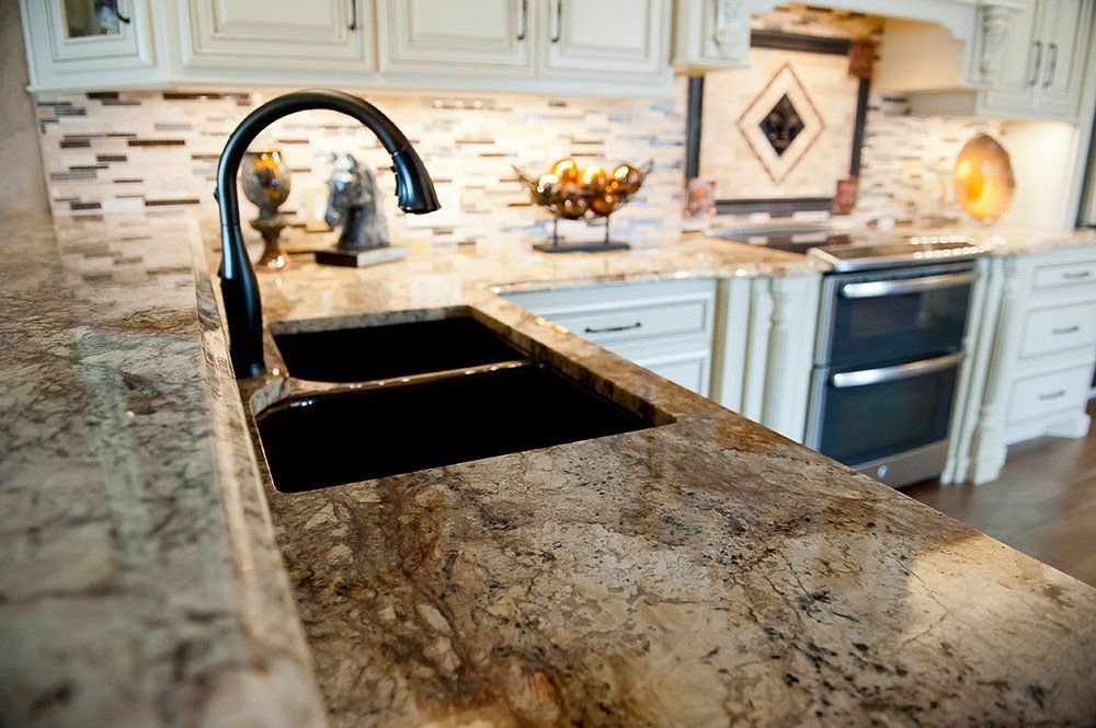 Modern kitchen with granite island, black sink and faucet, cream cabinets, and stainless steel oven