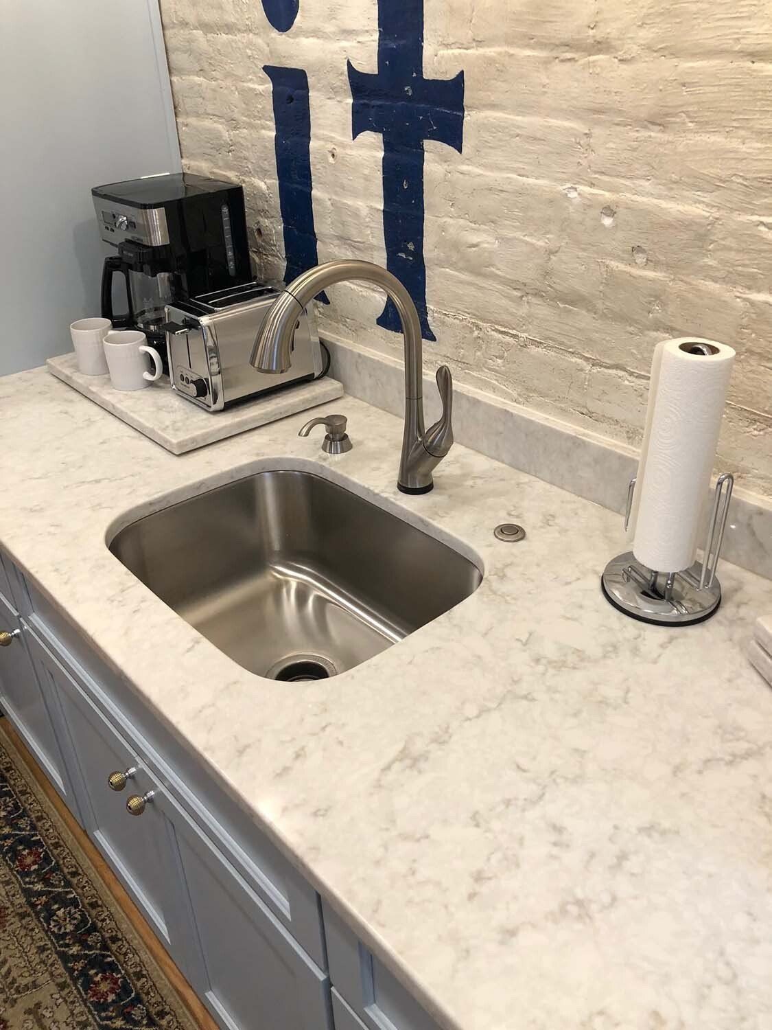 Modern kitchen sink with chrome faucet, soap dispenser, coffee maker, and paper towel roll on marble countertop