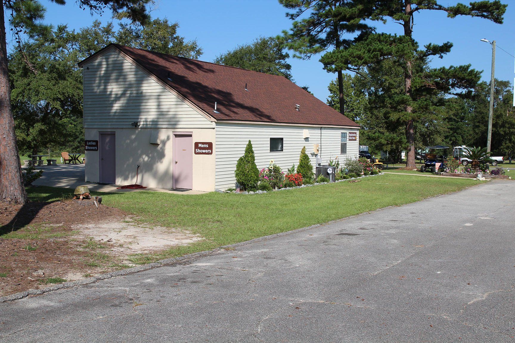A light-colored building with a brown roof and a small garden, likely a public restroom, at a campsite.