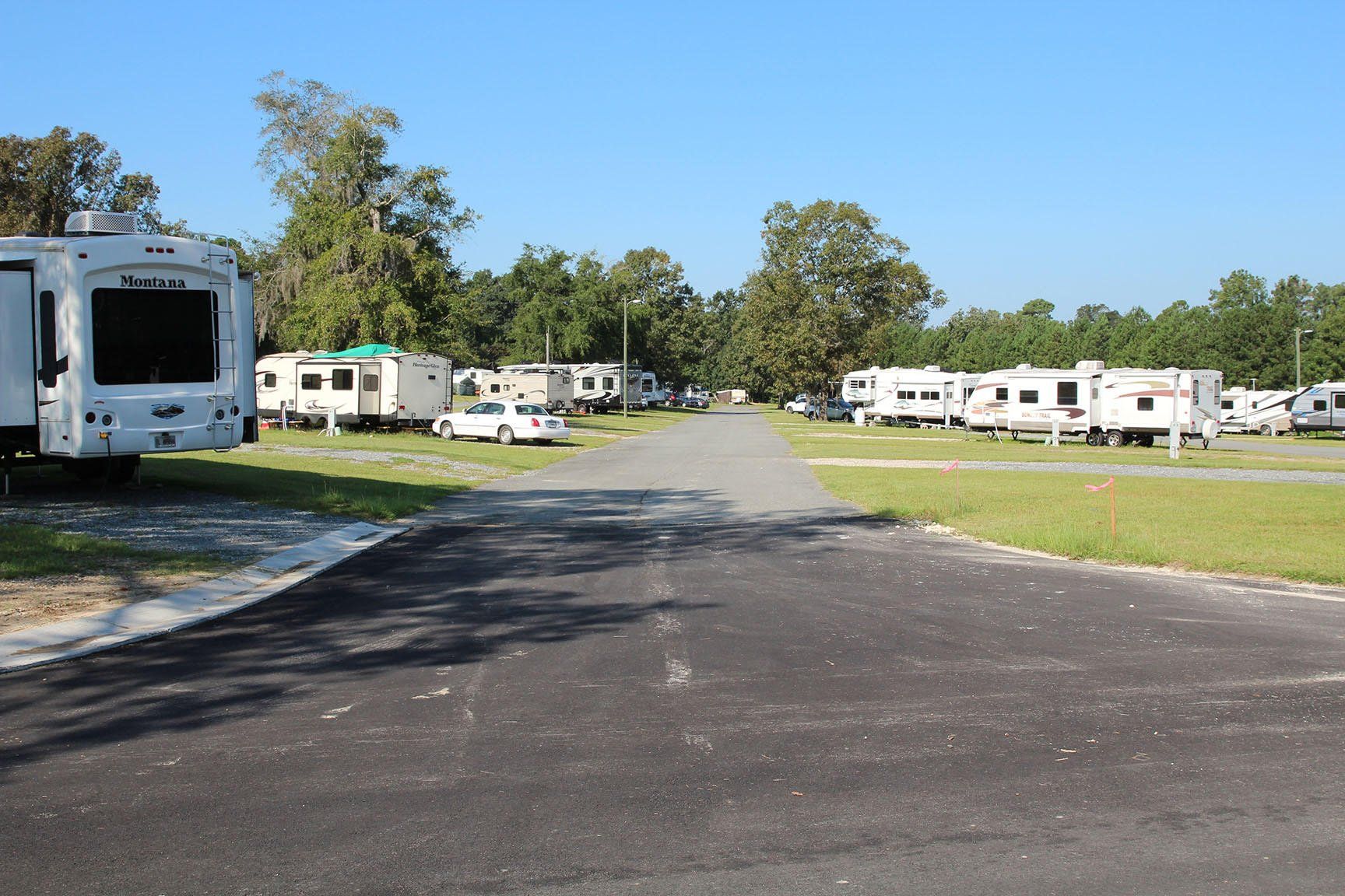 RV park with paved road and parked RVs on grass, under blue sky.