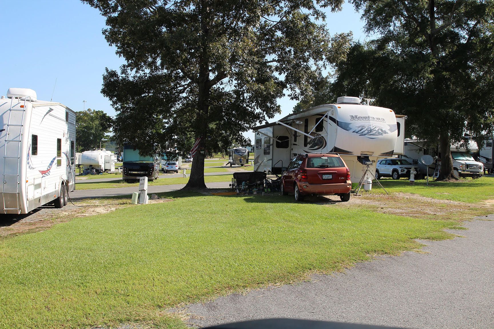 Campground with RVs parked on grassy lots, trees, and cars.
