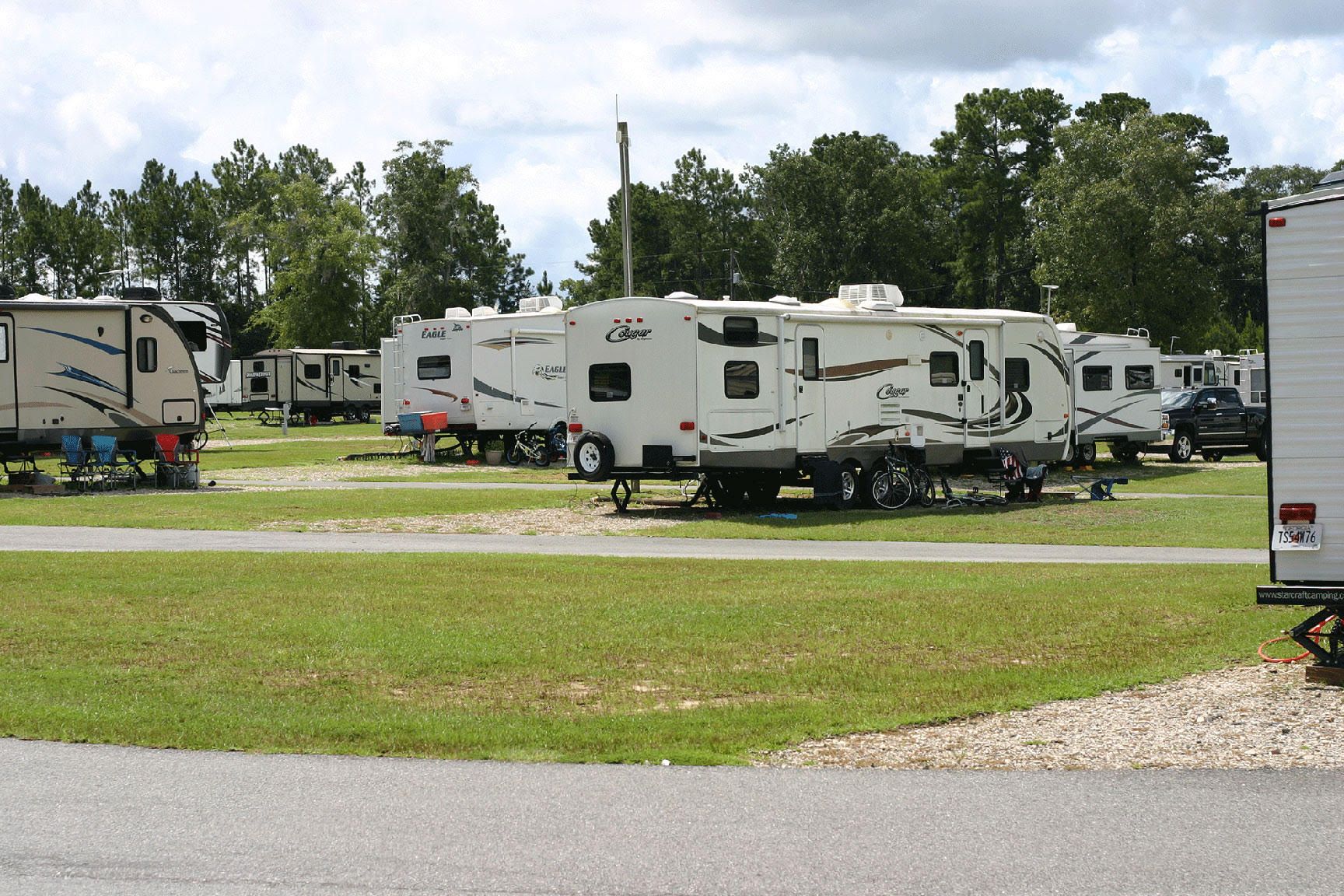 Campground with several RV trailers parked on grassy sites, sunny day.