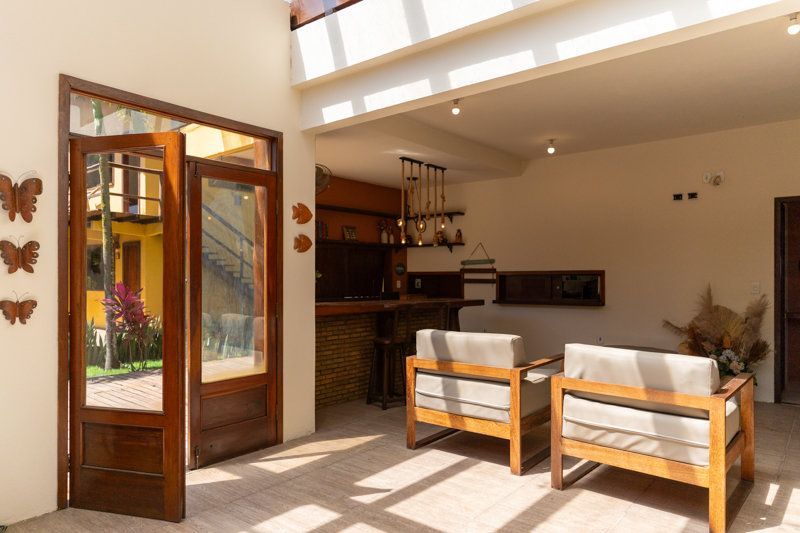 Pátio luminoso com portas de madeira abertas, duas cadeiras almofadadas e um pequeno bar num pátio ensolarado.