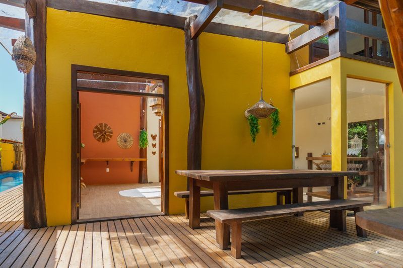Pátio rústico com paredes amarelas, bancos de madeira e uma porta aberta para um quarto laranja.