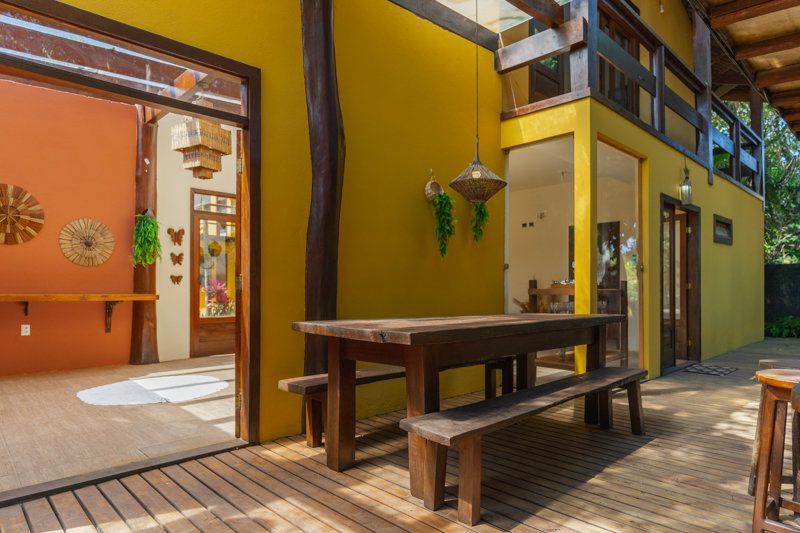 Pátio externo colorido com mesa de piquenique de madeira, porta aberta e paredes amarelo-alaranjadas.