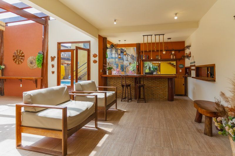 Sala de estar aconchegante com cadeiras de madeira, balcão de bar e luz natural abundante vinda da cozinha.