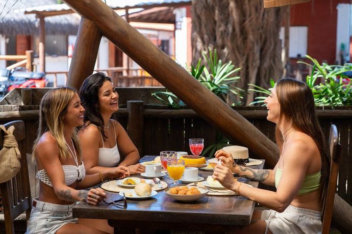 Três pessoas conversando em uma mesa de café ao ar livre, tomando café da manhã e bebidas.