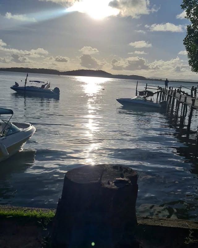 Porto ensolarado com barcos ancorados, águas ondulantes e uma ilha baixa no horizonte ao pôr do sol.