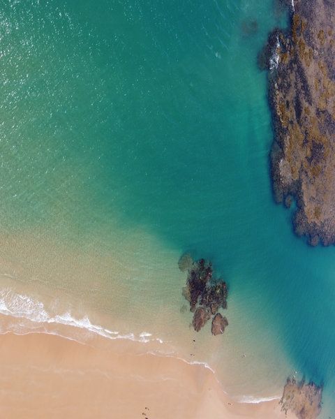 Vista aérea de uma praia de areia com água turquesa e costa rochosa.