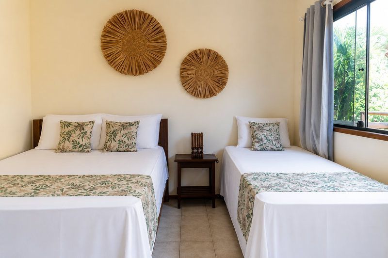 Quarto luminoso com duas camas de solteiro, roupa de cama branca, decoração de parede em tecido e janela com cortinas.
