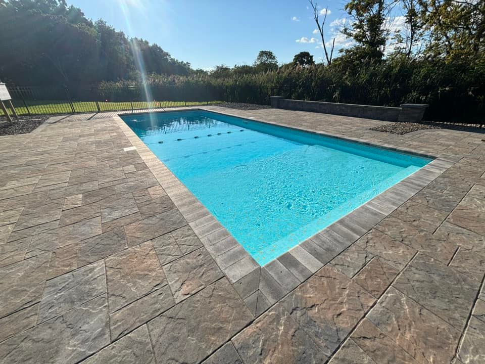 Rectangular pool with turquoise water, surrounded by stone pavers, sunny outdoor setting.