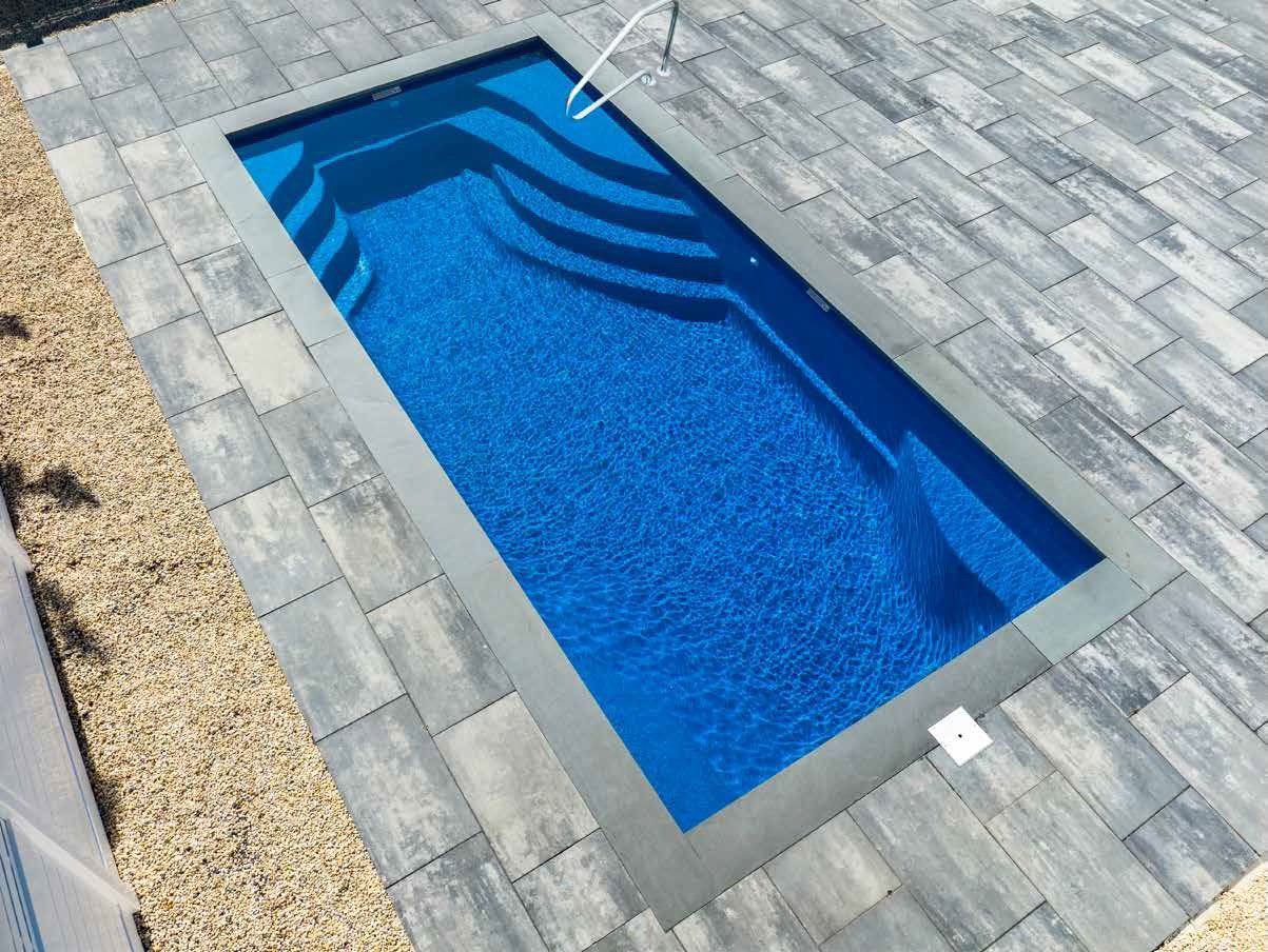 Rectangular blue pool with steps, surrounded by gray paving stones and a gravel border.