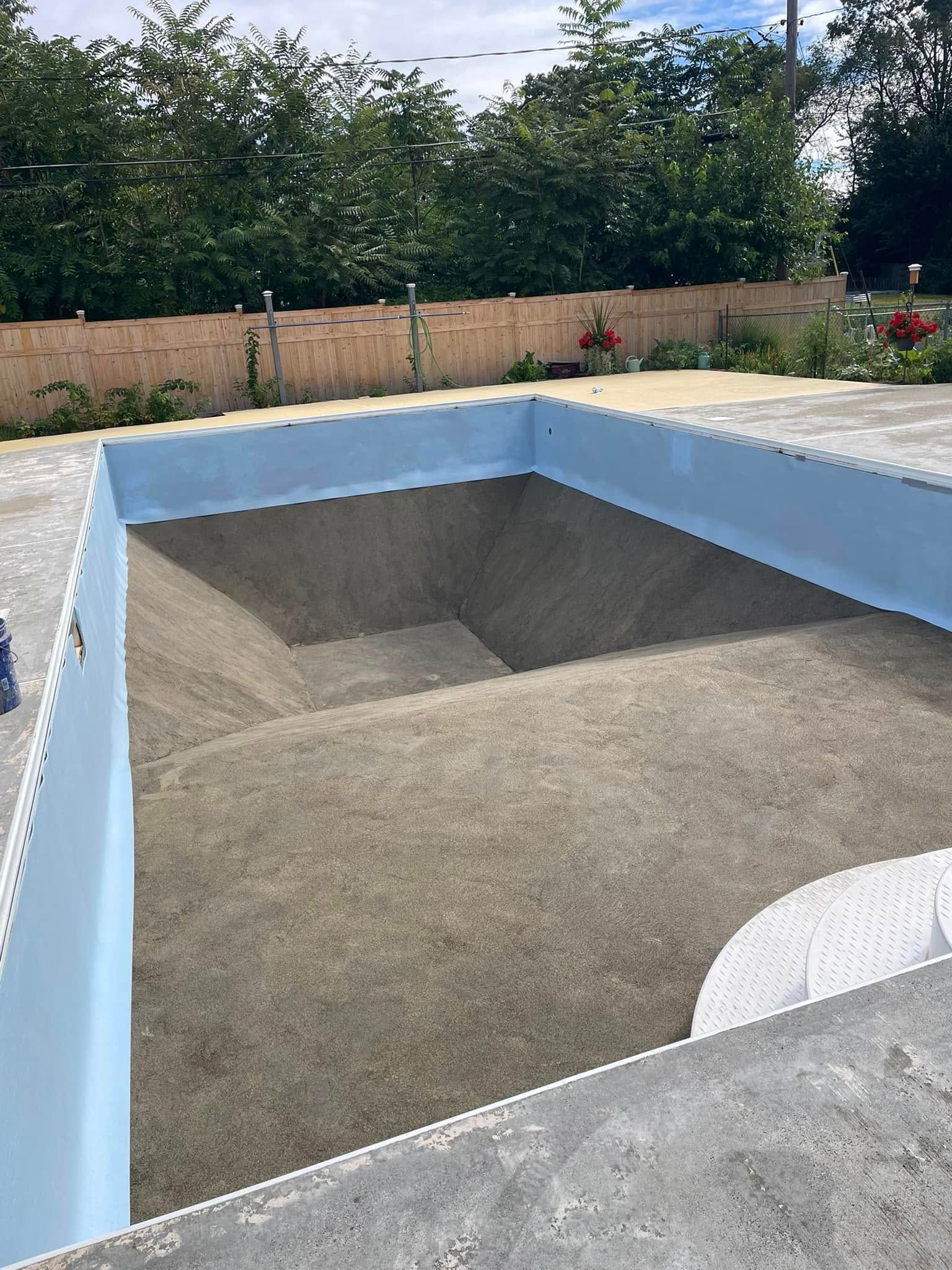 Empty swimming pool with blue lining, filled with sand, steps visible.