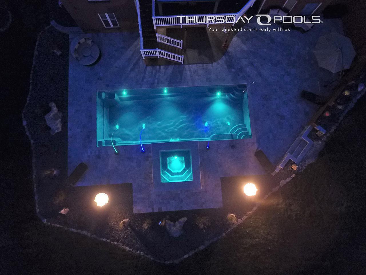 Aerial night view of a lit swimming pool with blue water and surrounding patio lights