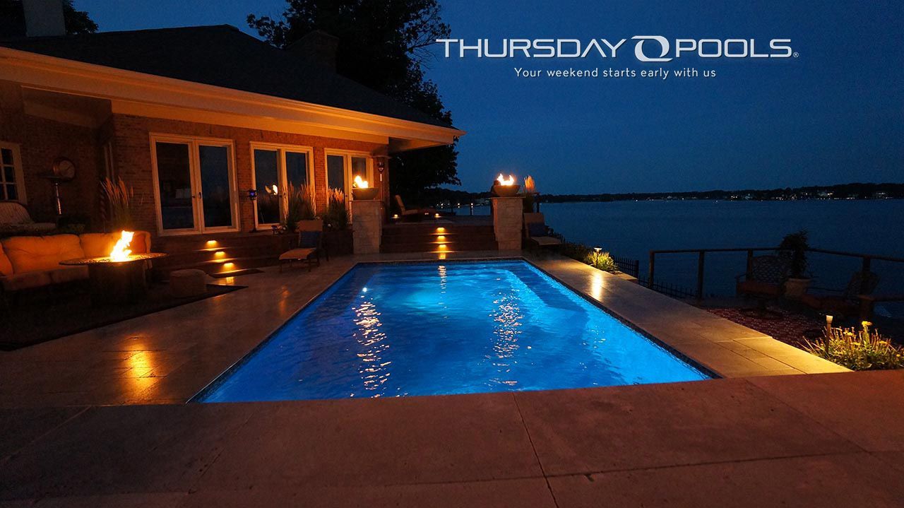 Luxury backyard pool at dusk beside a lit house, overlooking a calm lake