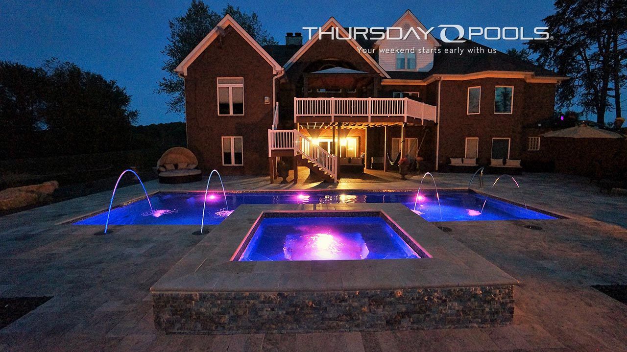 Large brick house with a lit backyard pool and colorful LED water features at dusk