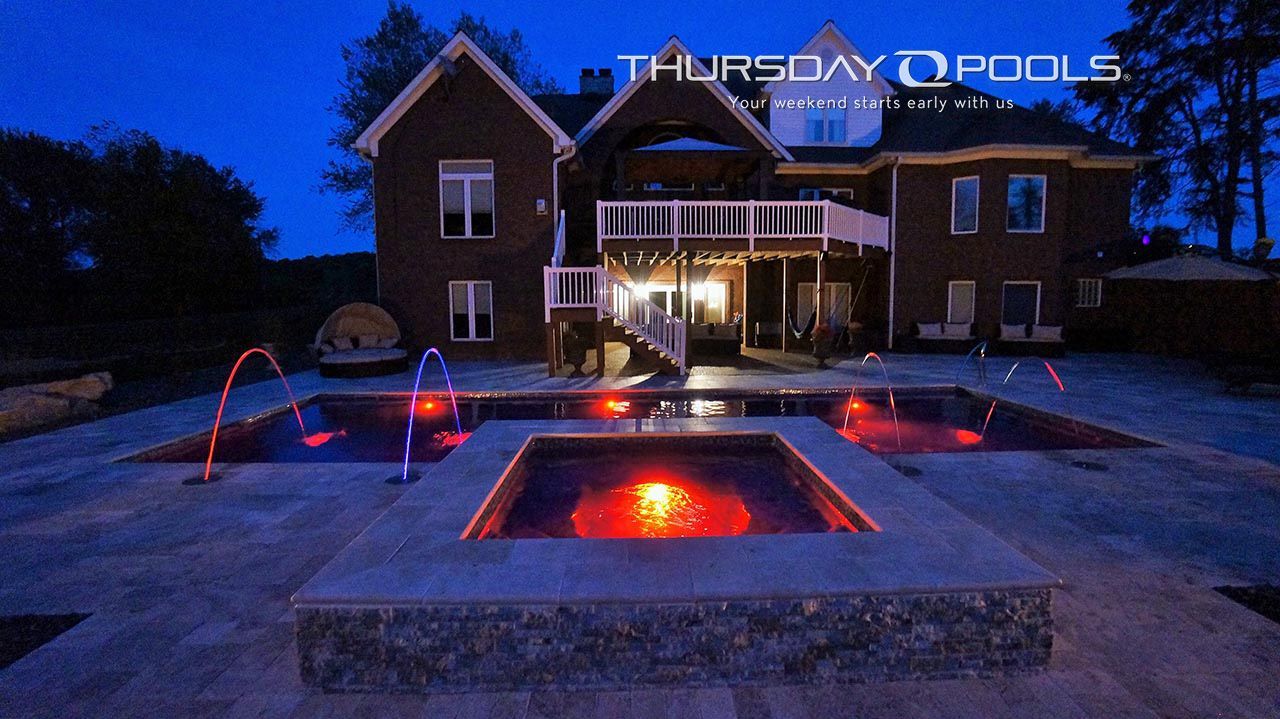 Modern brick house with a lit pool and fire feature at dusk, blue sky and patio seating