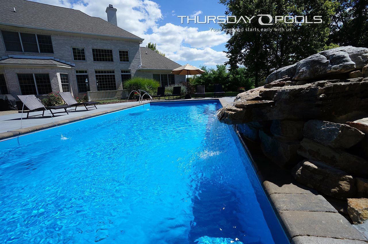 Backyard pool beside a stone waterfall and a house on a sunny day