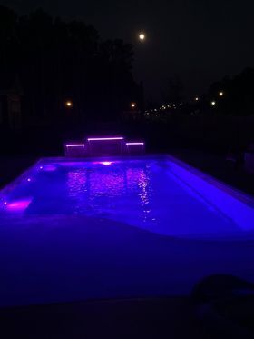 Blue-lit swimming pool at night with a glowing waterfall and reflections on the water