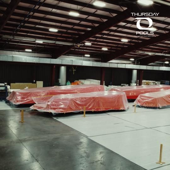 Covered red equipment in a warehouse-like hall with concrete floor and overhead lights