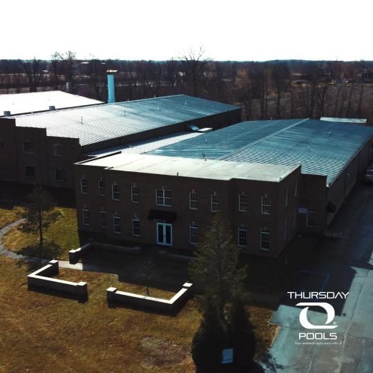 Aerial view of a large brick building with a gray metal roof on a grassy lot.