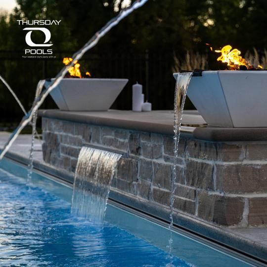 Modern pool with stone water feature and lounge chairs at dusk