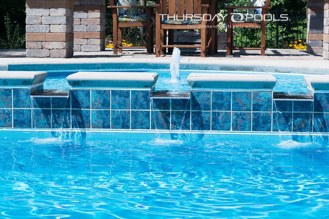 Blue swimming pool with tiled edge and a small fountain in front of a building entrance