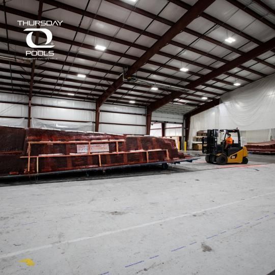 Warehouse interior with a forklift beside a large red metal structure on a concrete floor