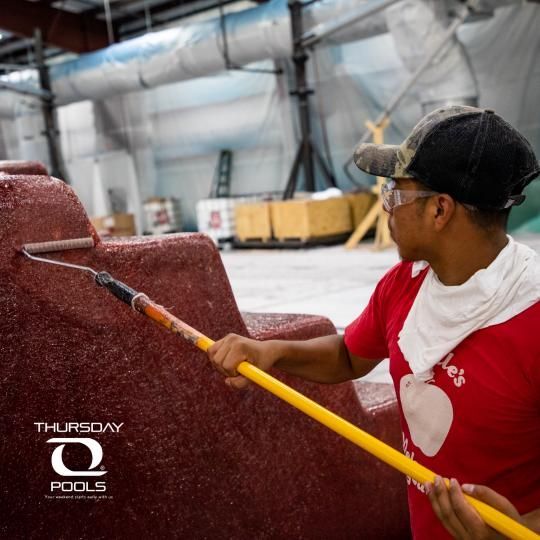 Worker using a long-handled brush to clean a red pool surface indoors