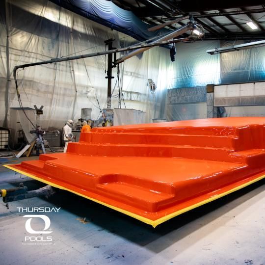 Large glossy orange pool shell in a factory workshop, with “Thursday Pools” watermark in the corner