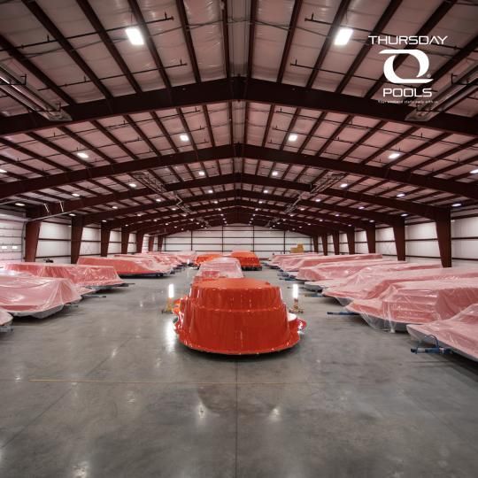 Warehouse interior with rows of red plastic-wrapped equipment on pallets under a high metal roof