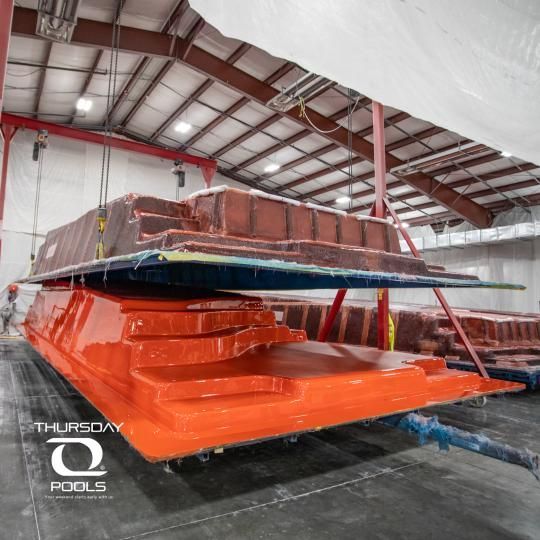 Orange boat hull and covered equipment stacked in a warehouse with metal beams and concrete floor
