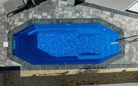 Blue pool with gray brick border surrounded by light-colored paving stones.