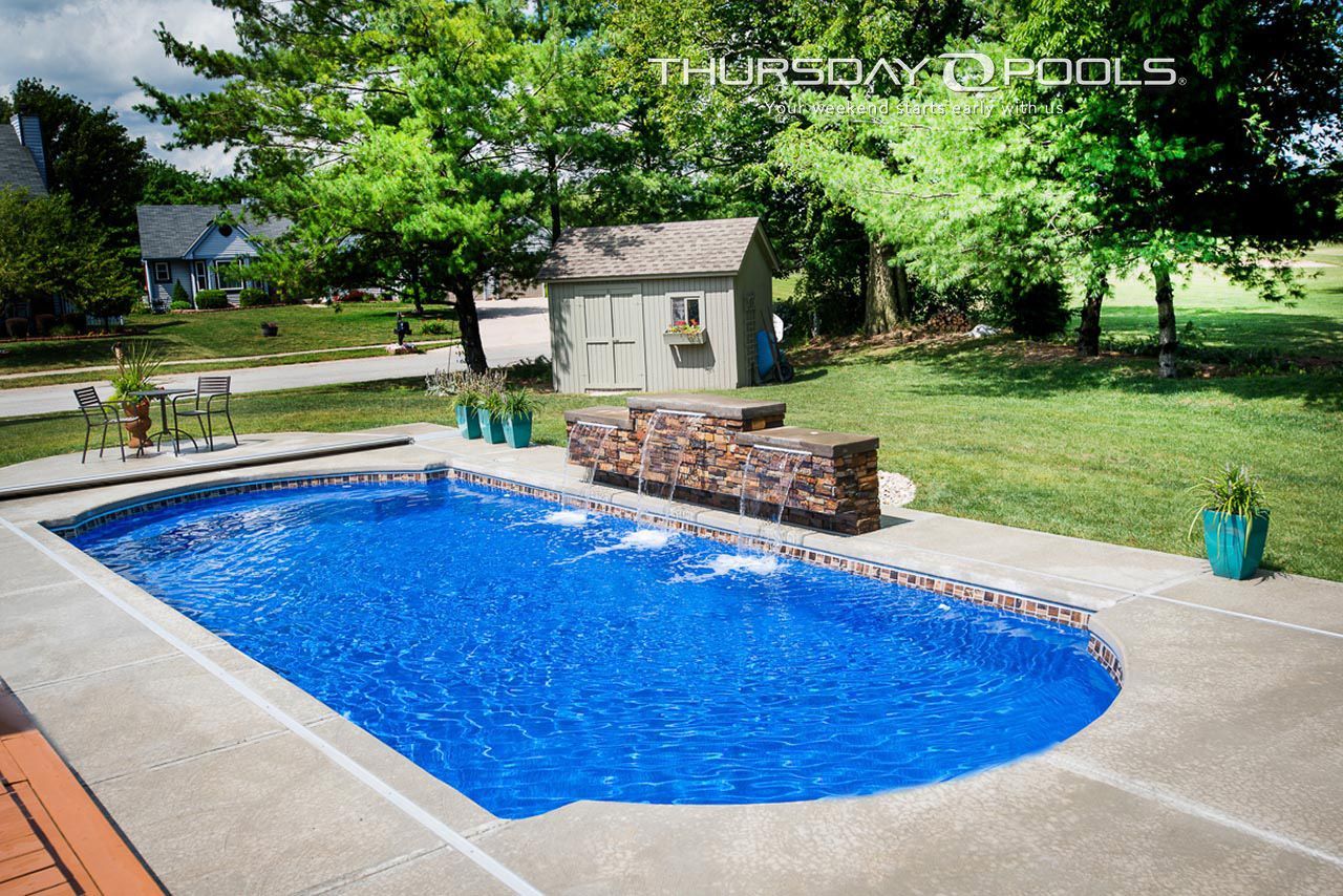 Backyard swimming pool with bright blue water, stone waterfall feature, and surrounding trees