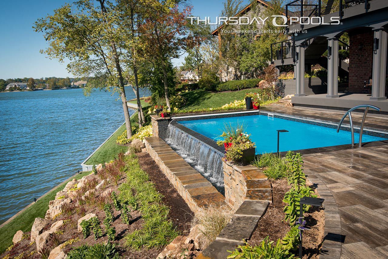 Lakeside patio with a small blue pool beside a brick house and garden
