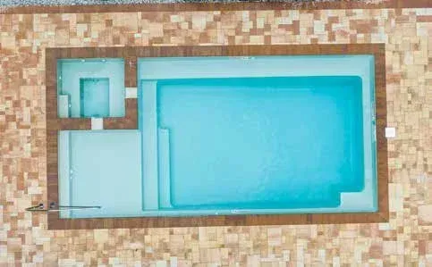 Overhead view of a rectangular swimming pool with varying depths, surrounded by light-colored tiled patio.