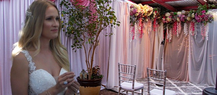 A woman in a wedding dress is standing in front of a flower arrangement.