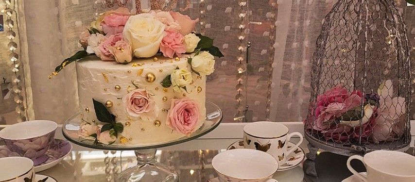 A cake with flowers on it is sitting on a table next to tea cups and saucers.