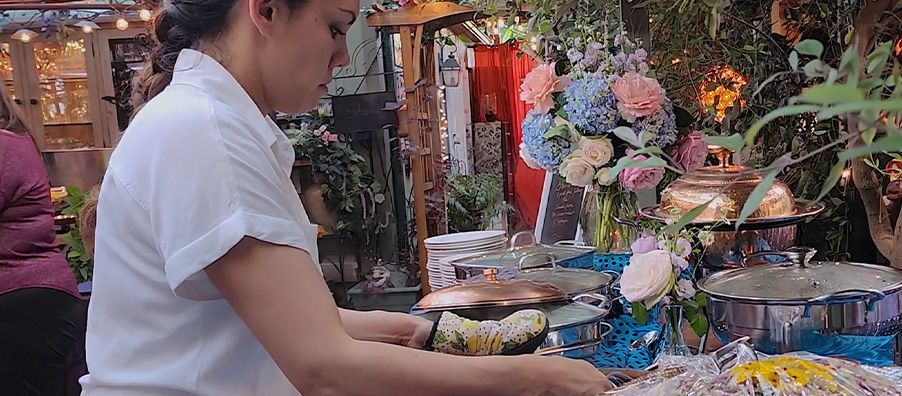 A woman in a white shirt is preparing food at a buffet table.