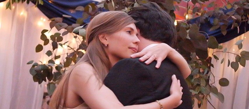 A woman is hugging a man in front of a tree.