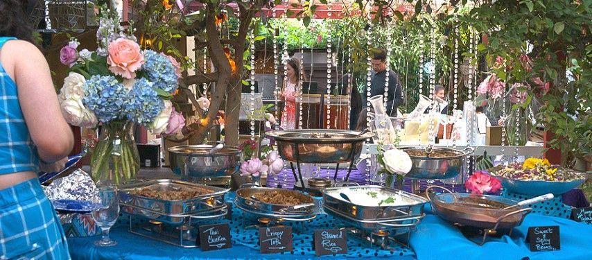 A woman is standing in front of a table filled with food and flowers.