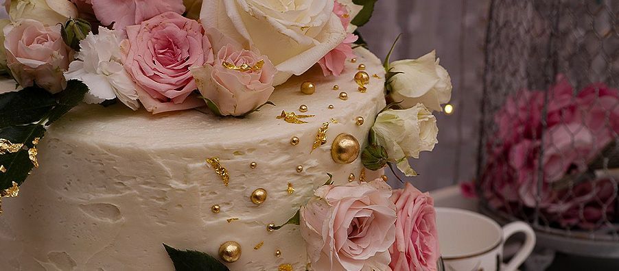 A wedding cake decorated with pink roses and gold sprinkles.