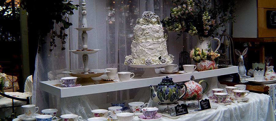 A table with a cake , teapots , cups and saucers on it.