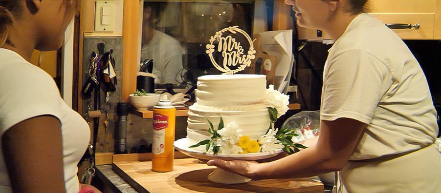 Two women are preparing a wedding cake in a kitchen.