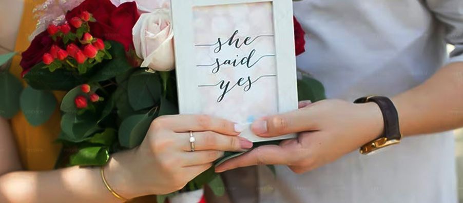 A man and a woman are holding a sign that says `` she said yes ''.