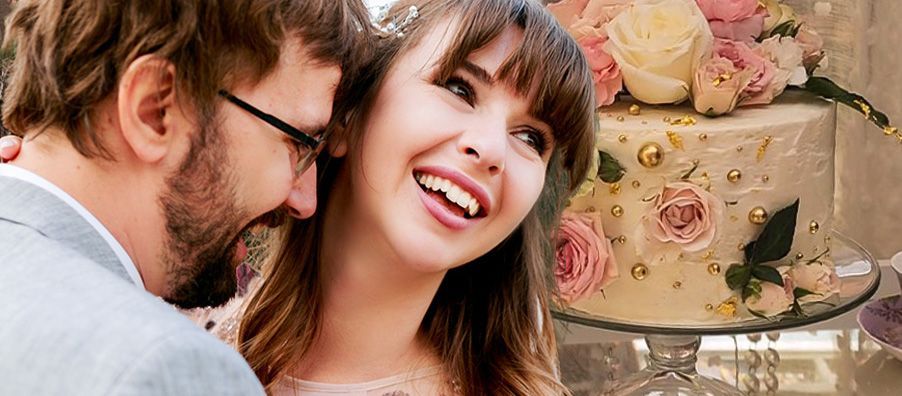 A bride and groom are smiling in front of a wedding cake.
